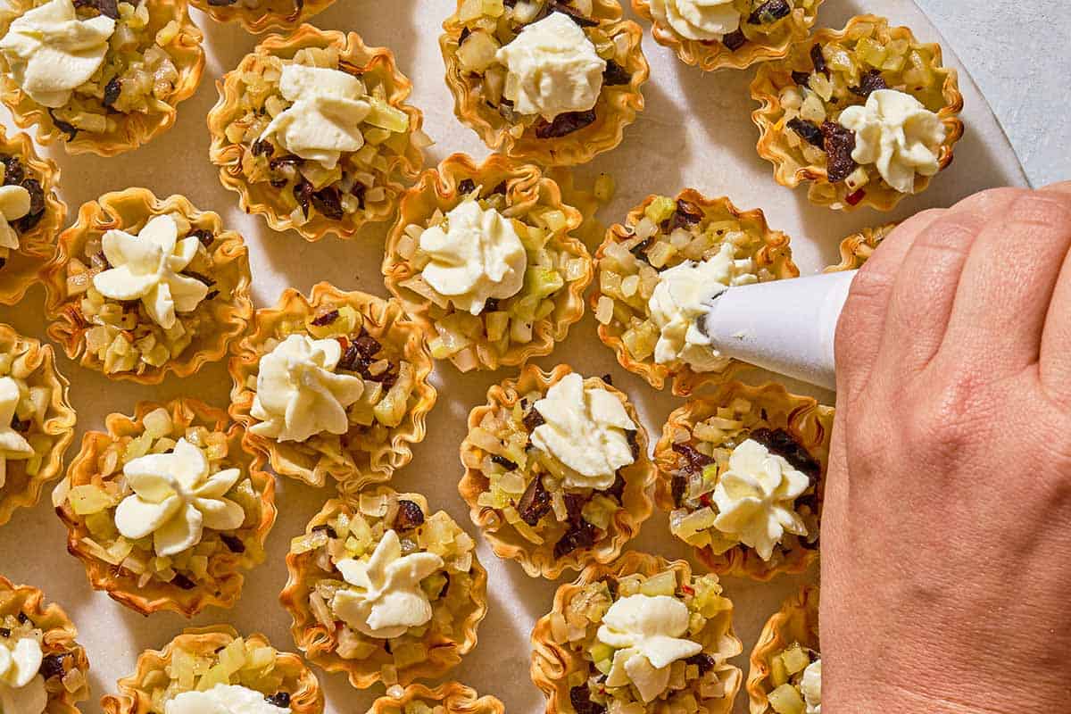The goat cheese mixture being piped onto the phyllo cup appetizers on a platter.