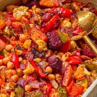 Oven roasted vegetables in a baking dish with a serving spoon.