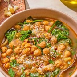 A serving of spinach soup in a bowl with a spoon. Next to this is a block of pecorino Romano cheese, a cheese grater, and a bottle of olive oil.