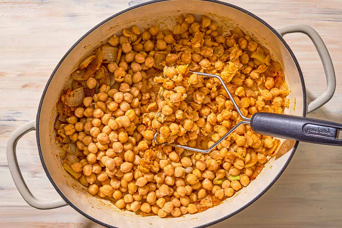 The chickpea mixture for the spinach soup being mashed in a pot.
