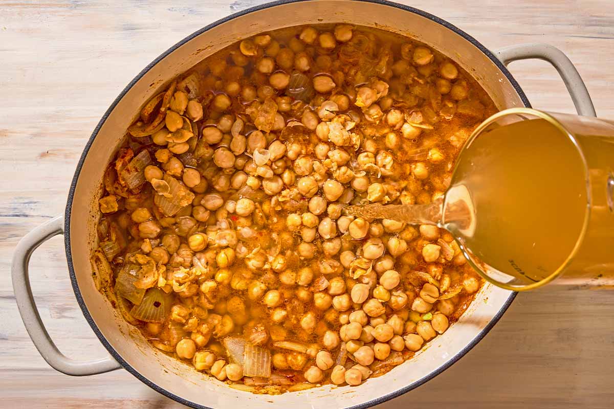 The liquids for the spinach soup being added to the pot of seasoned chickpeas and vegetables.