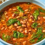 A serving of black eyed peas in a bowl next to a baguette.