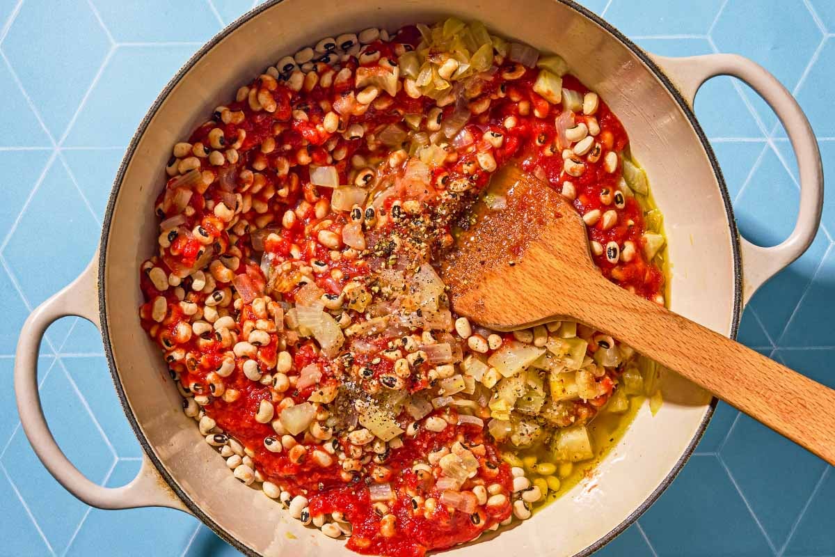 The ingredients for the black eyed peas being stirred together in a pot with a wooden spoon.