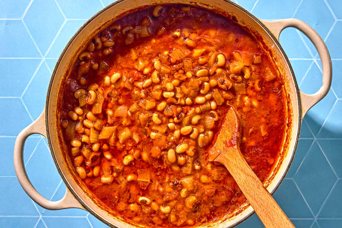 The ingredients for the black eyed peas being stirred together in a pot with a wooden spoon.