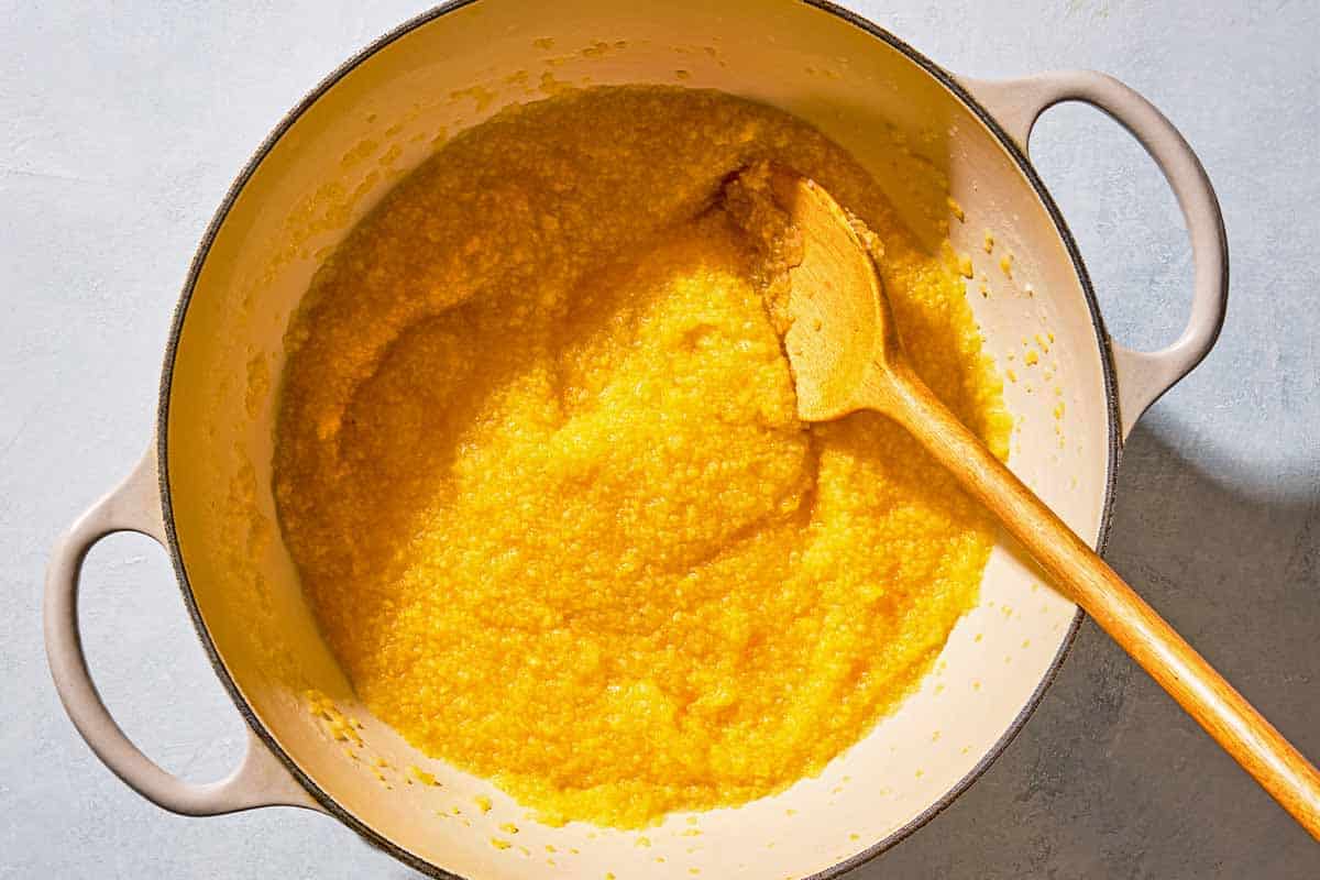 Polenta being stirred in a pot with a wooden spoon.