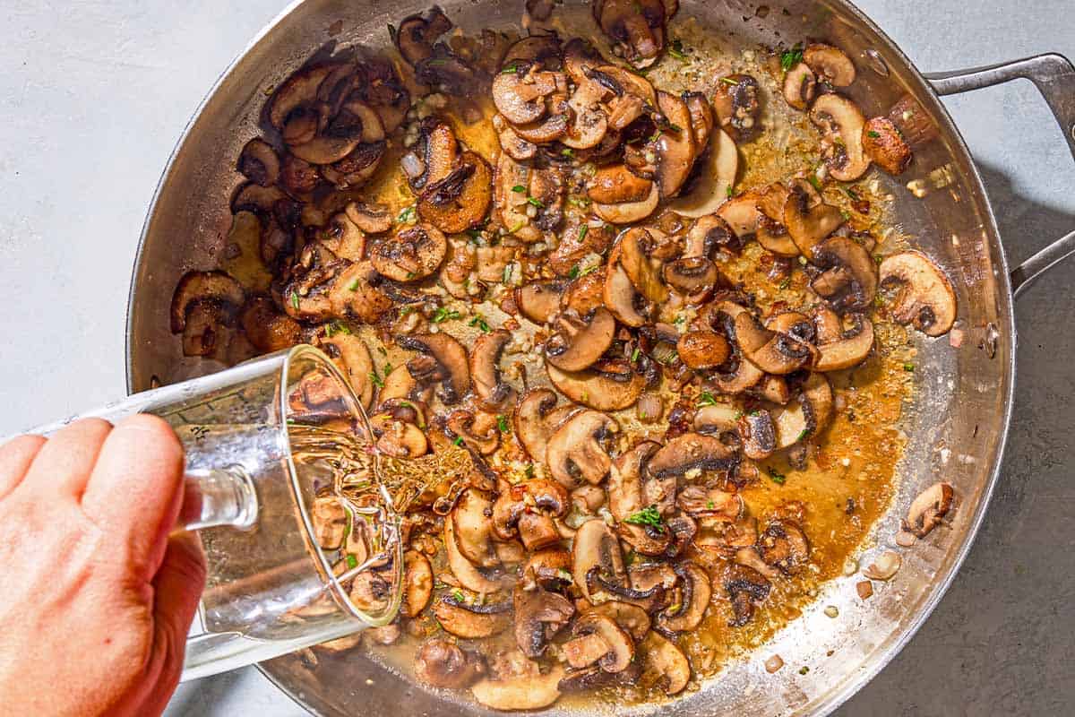 White wine being poured in the skillet with the sauteed mushrooms for the mushroom polenta.