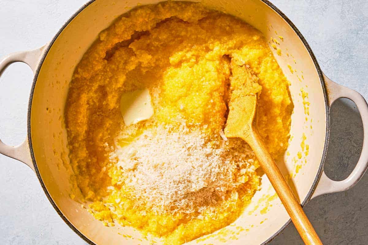The polenta, butter and parmesan cheese for the mushroom polenta in a pot with a wooden spoon.
