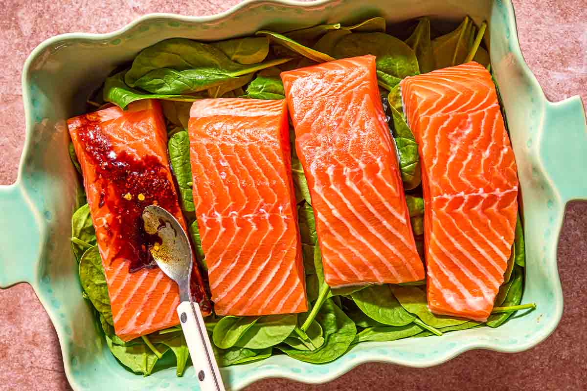 The glaze being added to the salmon fillets on a bed of spinach in a baking dish.
