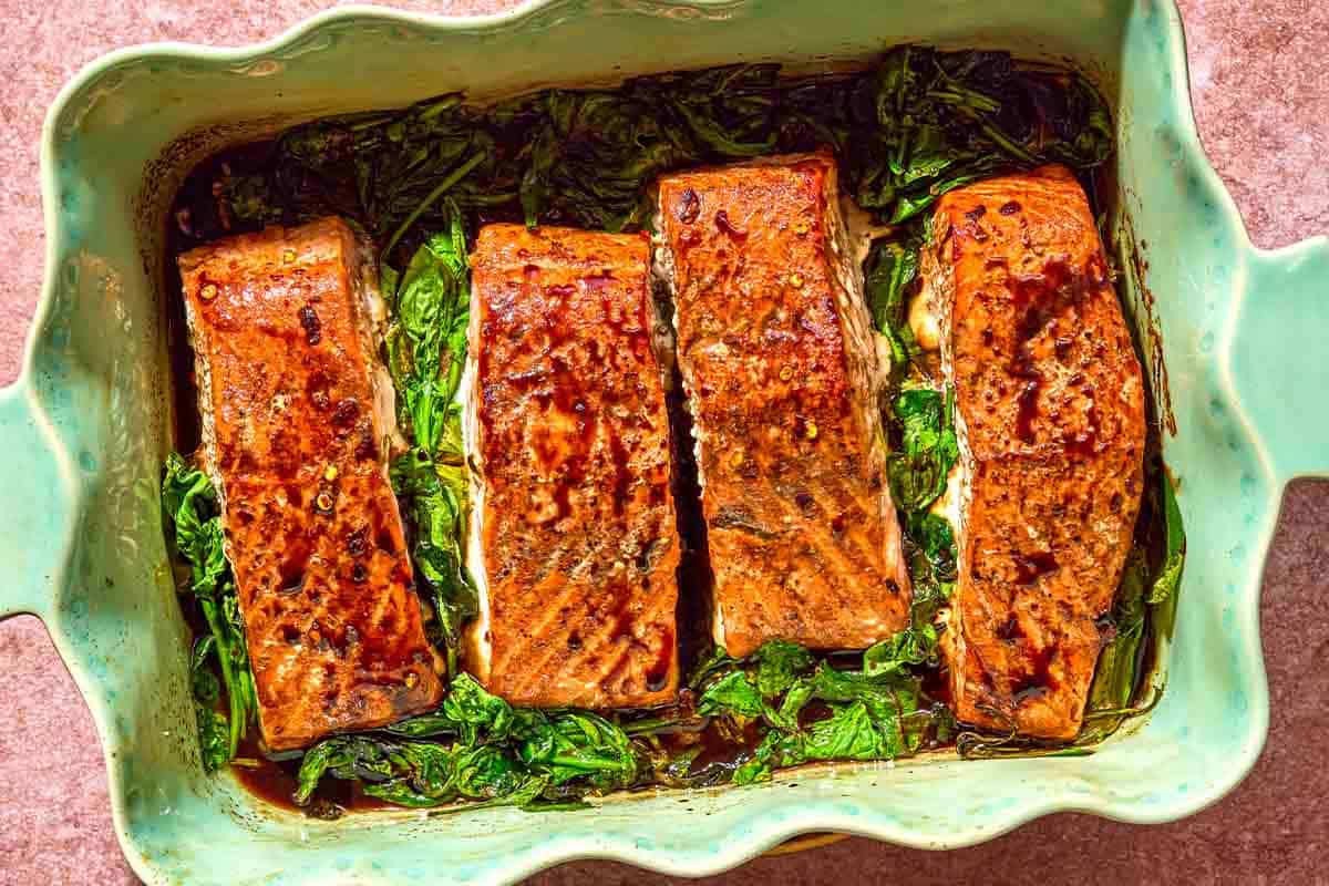 Glazed salmon fillets on a bed of baby spinach in a baking dish.