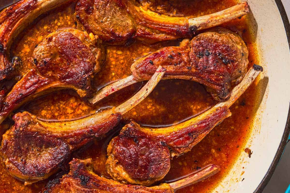 The lollipop lamb chops being cooked in a skillet.