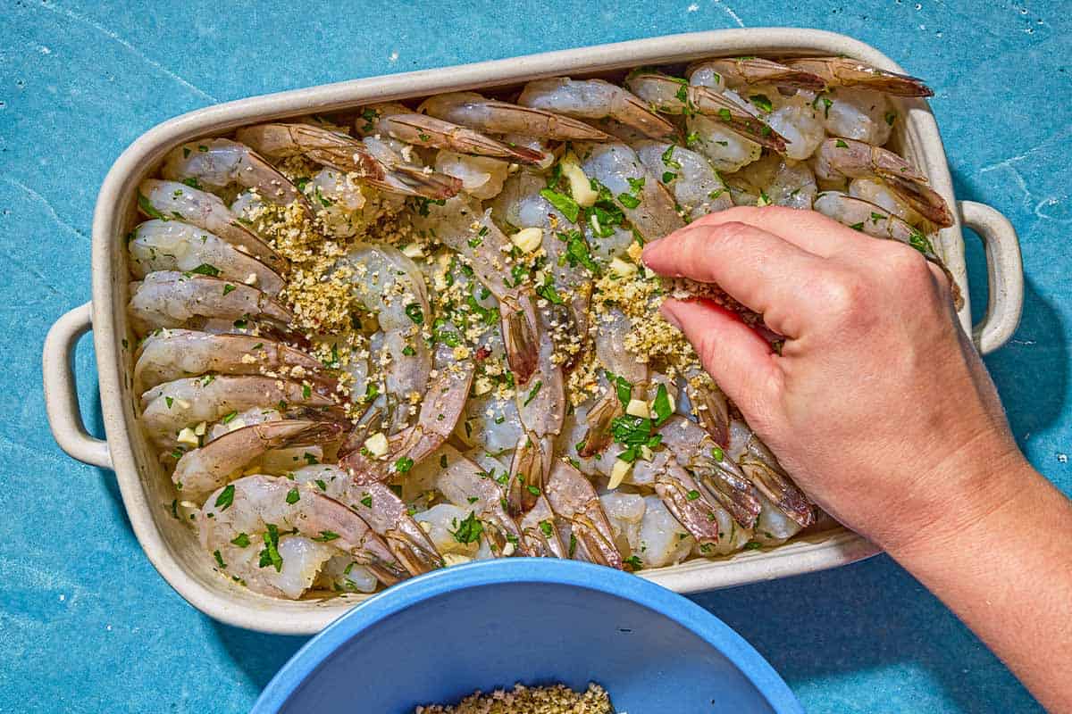 The oreganata being sprinkled over the uncooked shrimp mixture assembled in a baking dish.
