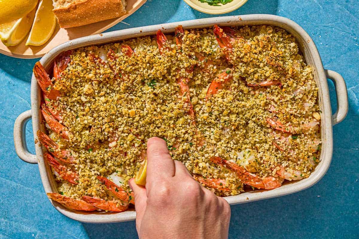 Lemon juice being squeezed onto the shrimp oreganata in a baking dish.