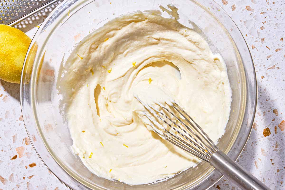 The ricotta dip being mixed in a bowl with a whisk. Next to this is a lemon and a zester.