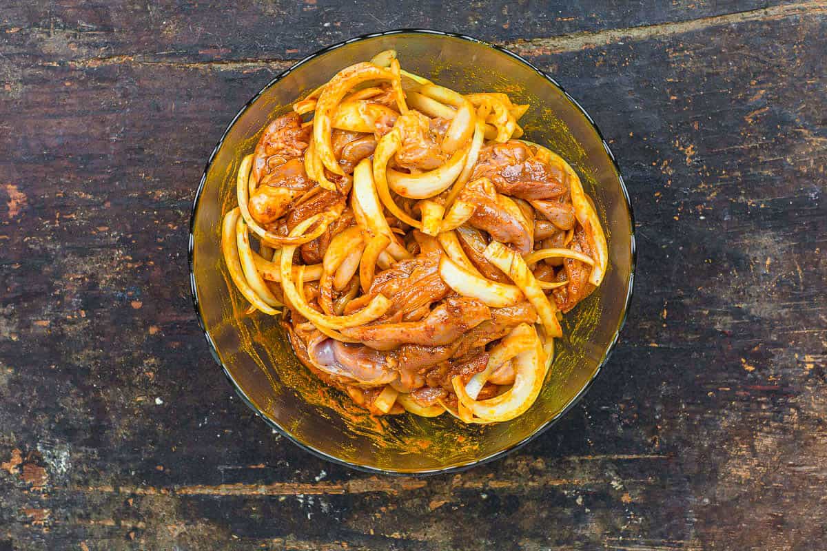 The chicken and onions for the chicken shawarma marinating in a bowl.