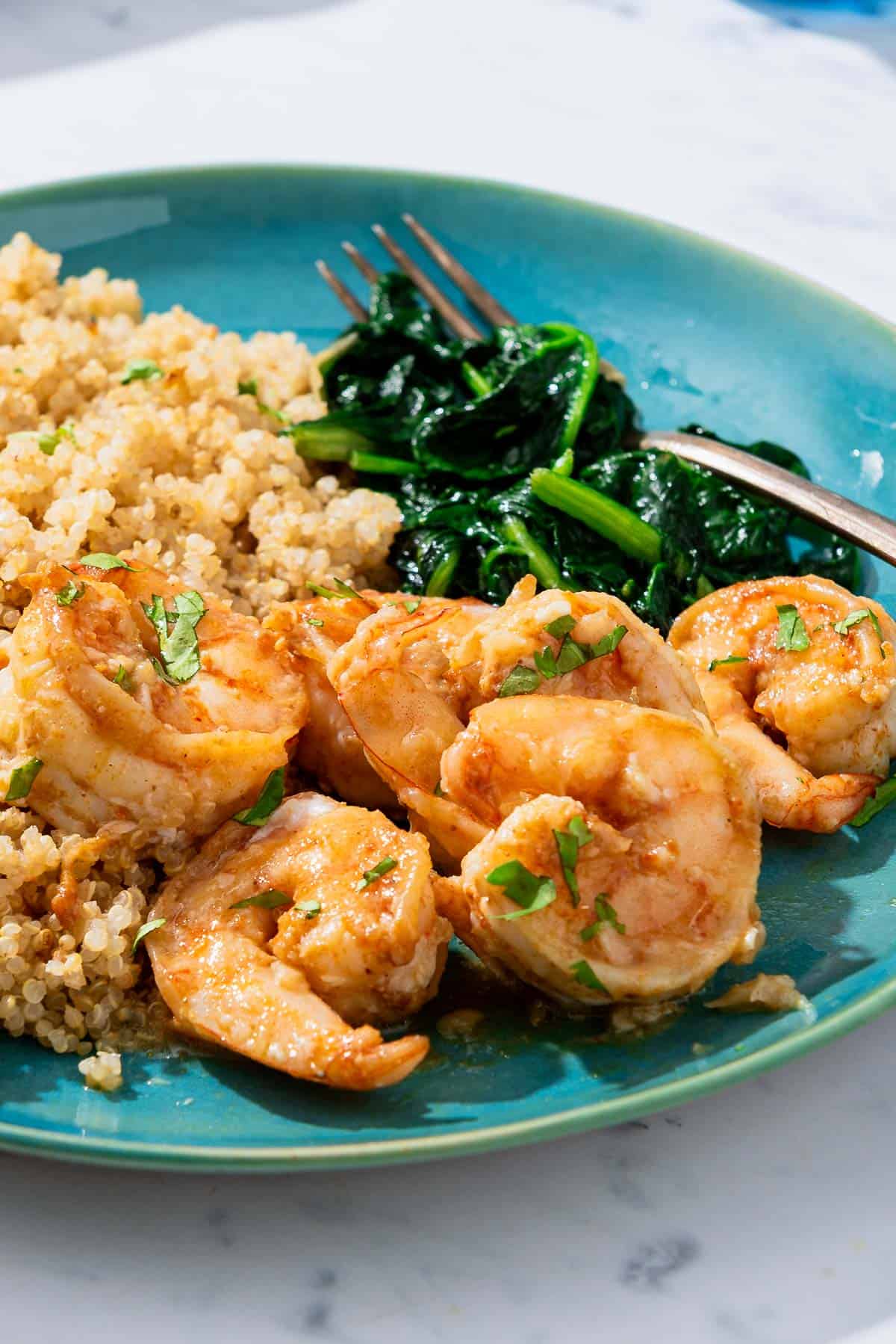A serving of the honey garlic shrimp on a plate with sides of couscous and saut&eacute;ed spinach and a fork.