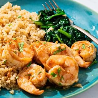 A serving of the honey garlic shrimp on a plate with sides of couscous and saut&eacute;ed spinach and a fork.