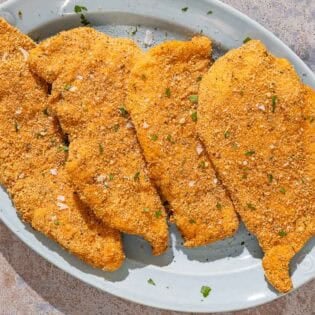 Four parmesan crusted chicken fillets on a platter.