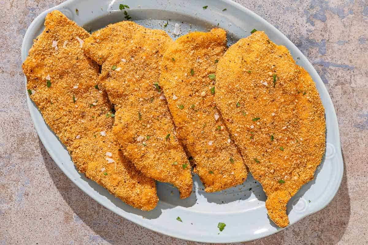 Four parmesan crusted chicken fillets on a platter.
