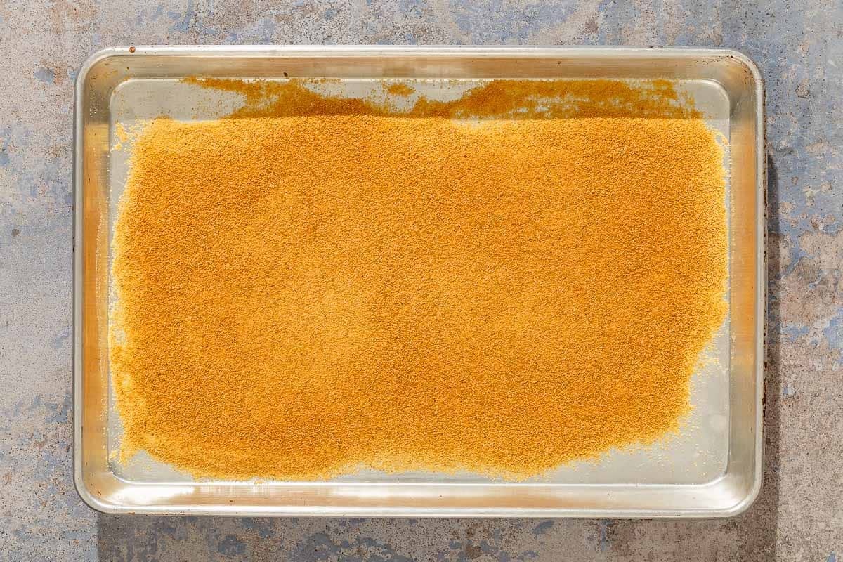 The toasted breadcrumbs for the parmesan crusted chicken spread evenly on a sheet pan.