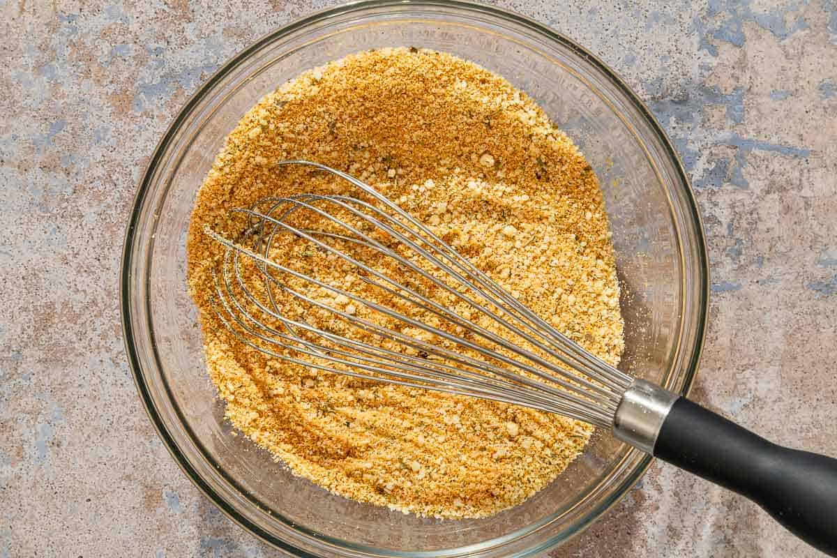 The bread crumbs mixed with the grated parmesan cheese and Italian seasoning in a bowl with a whisk.