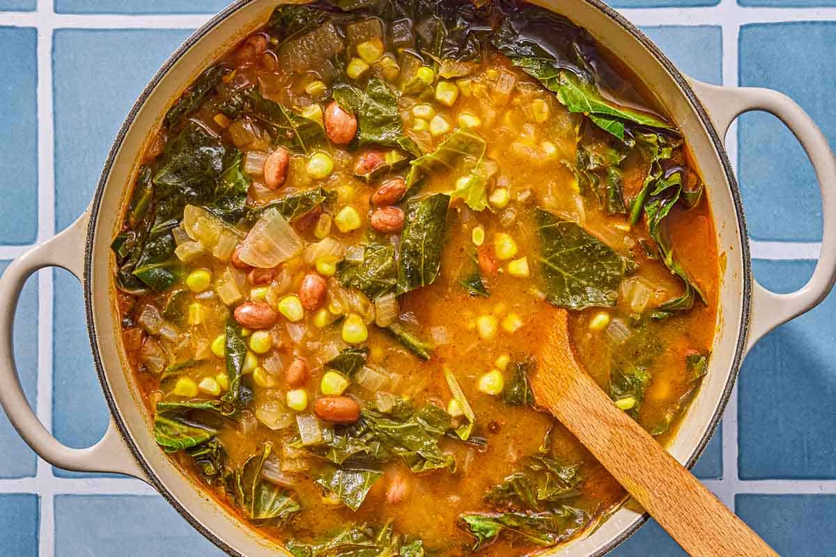 Collard green soup being stirred in a pot with a wooden spoon.