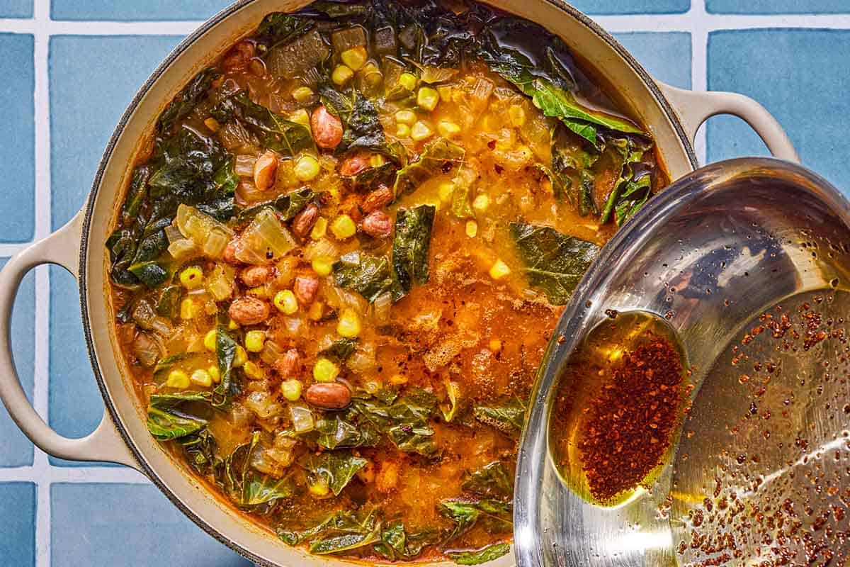 The Aleppo pepper sauce being poured over the collard green soup in a pot.