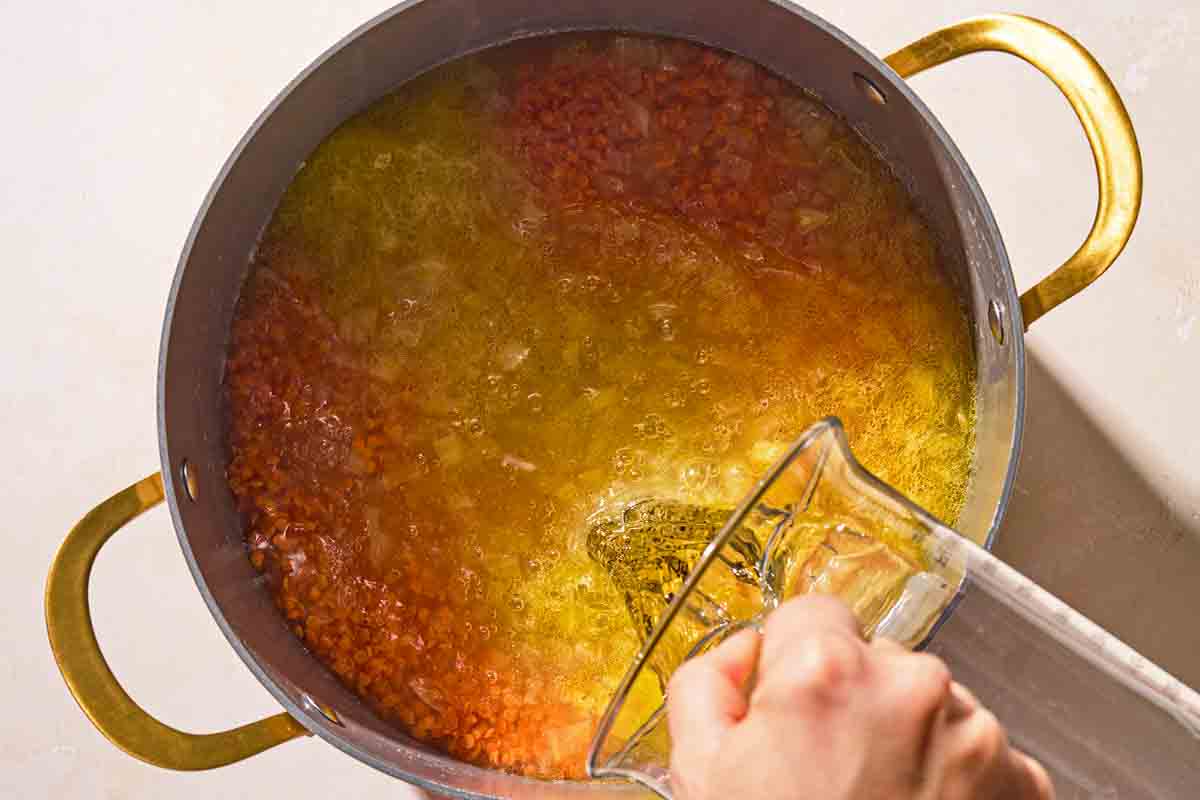 Hot water being poured over the red lentils for the Turkish lentil stew in a large pot.