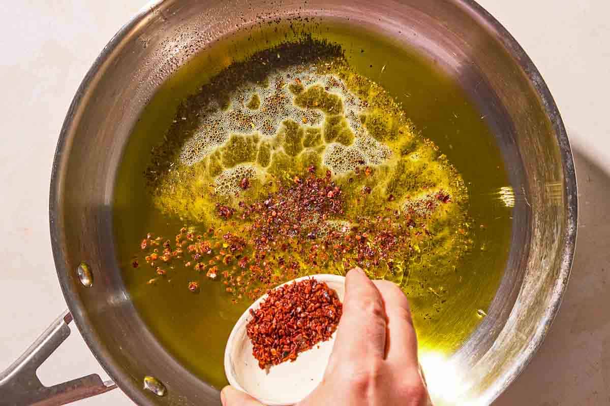 Aleppo pepper being added to olive oil in a skillet.