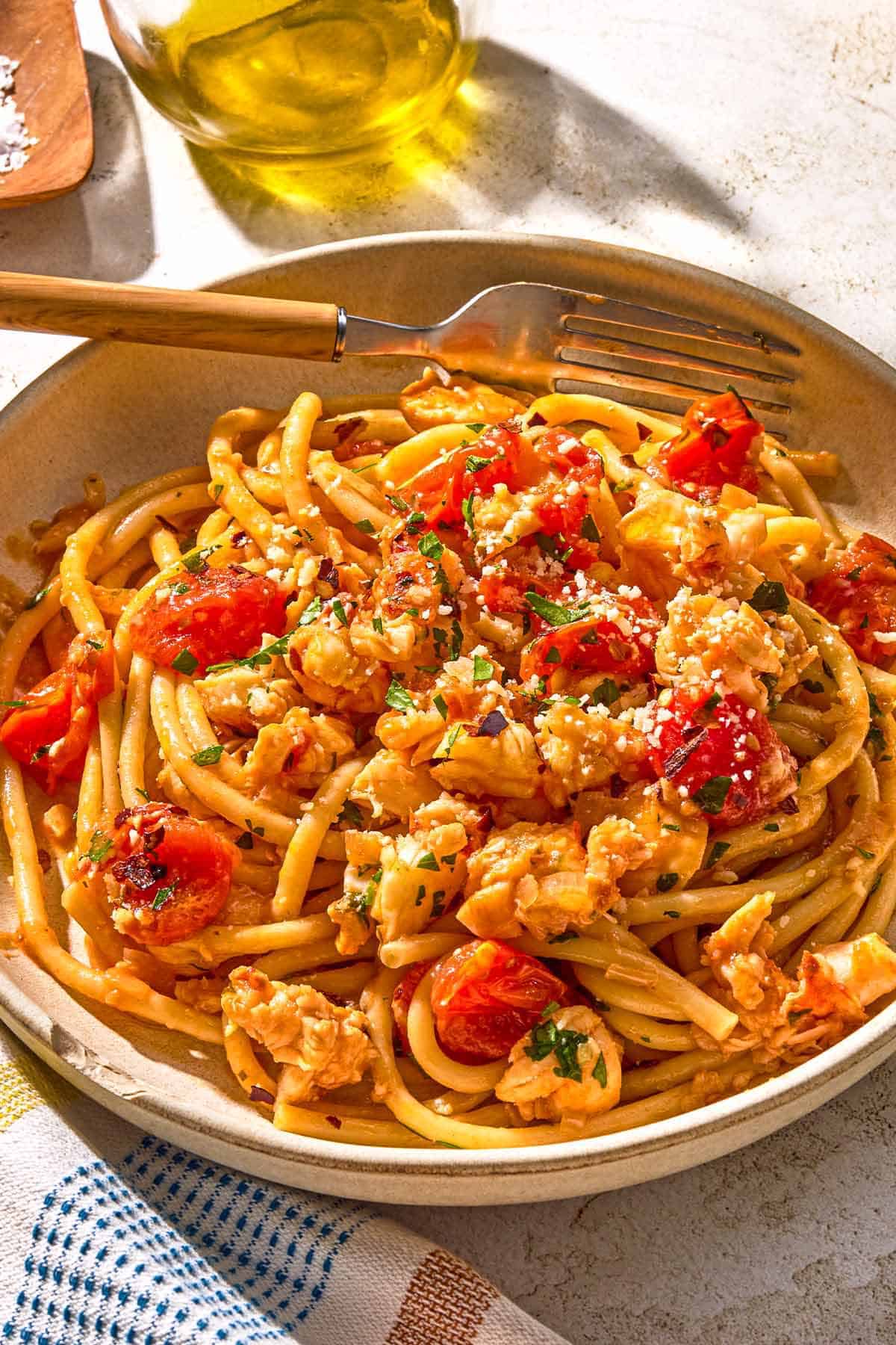Lobster pasta in a bowl with a fork next to a bottle of olive oil.