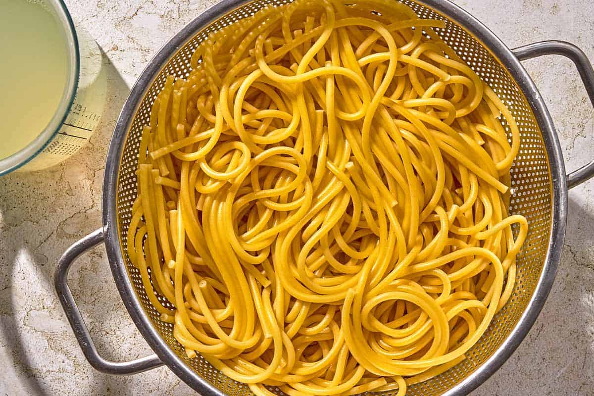 The pasta for the lobster pasta in a strainer next to a cup of pasta water.
