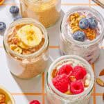 Four jars of overnight oats with various toppings. Next to these are raspberries, blueberries, almonds and a spoon.