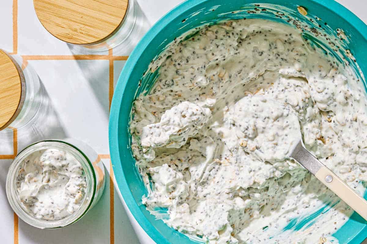The overnight oats in a mixing bowl with a spoon. Next to this is a jar of the overnight oats and two empty jars with lids.
