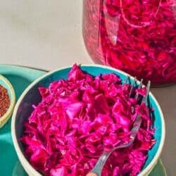 A bowl of pickled cabbage with a fork next to a jar of the pickled cabbage and a bowl of sumac.
