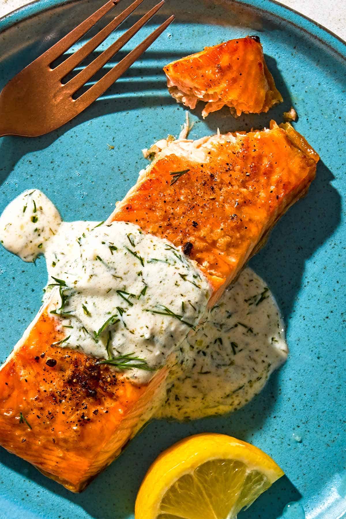 A serving of lemon dill salmon on a plate with a fork and a lemon wedge.