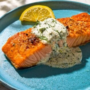 A serving of lemon dill salmon on a plate with a lemon wedge.