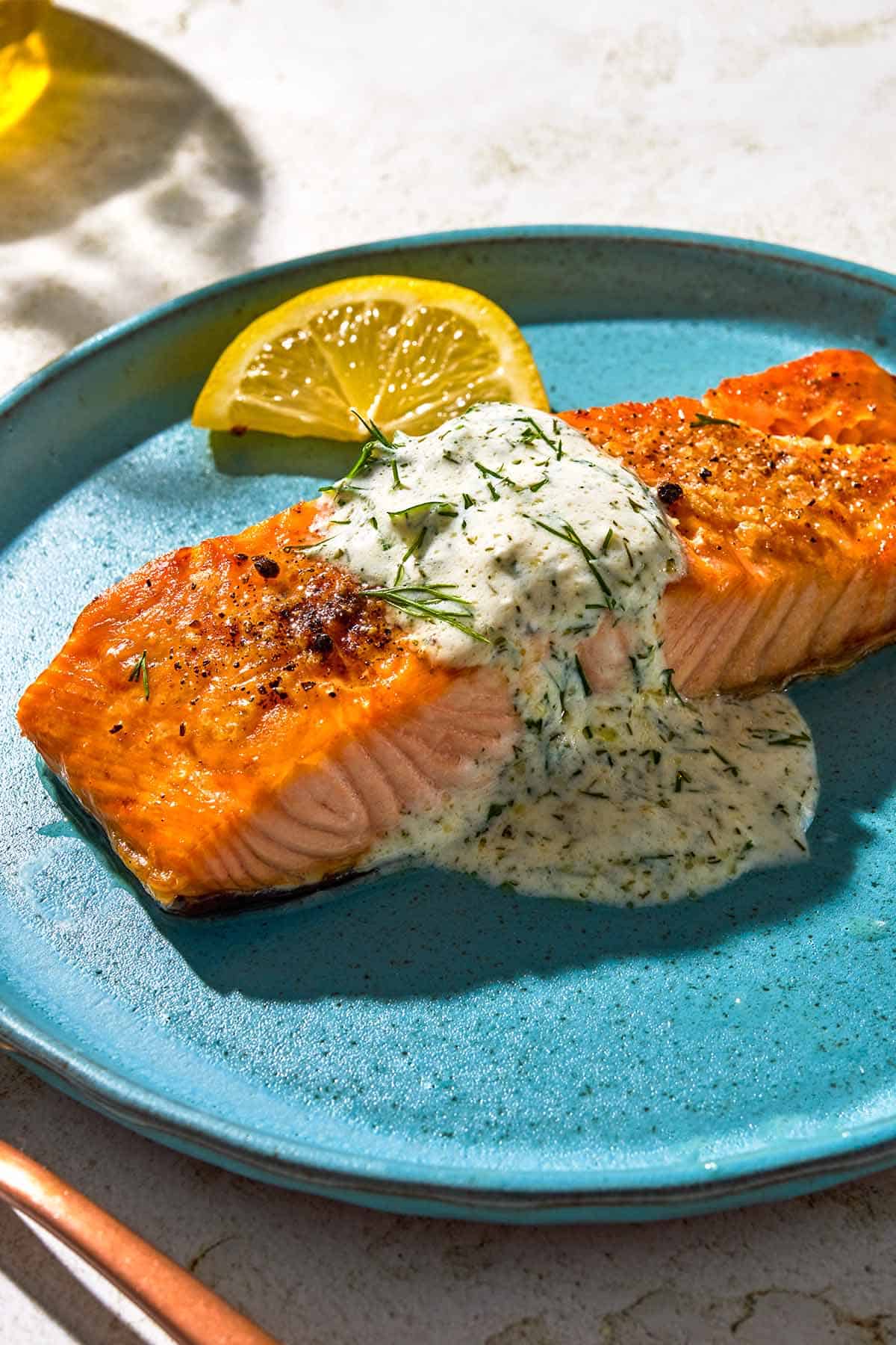 A serving of lemon dill salmon on a plate with a lemon wedge.