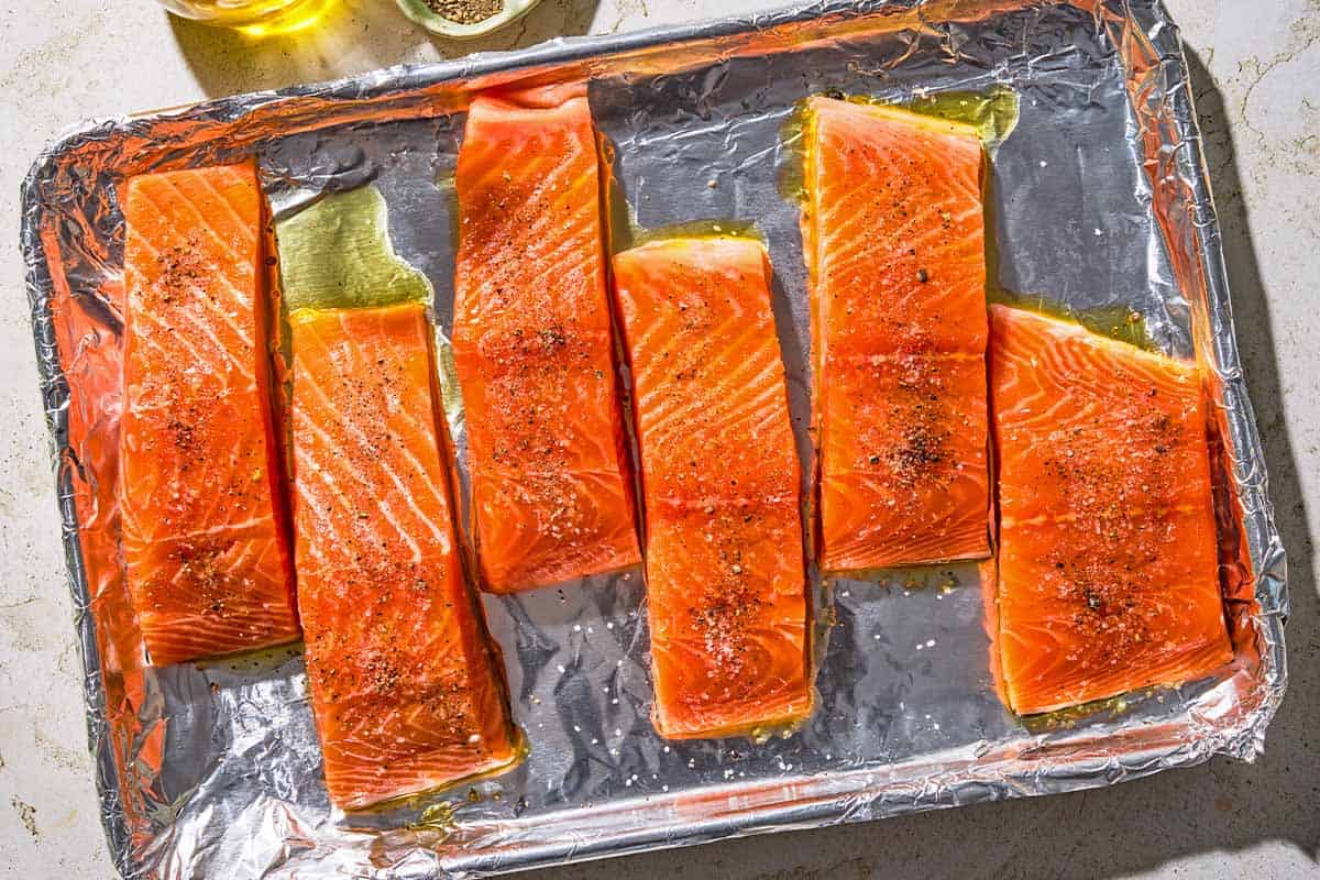 Six unbaked salmon fillets on a foil lined sheet pan.