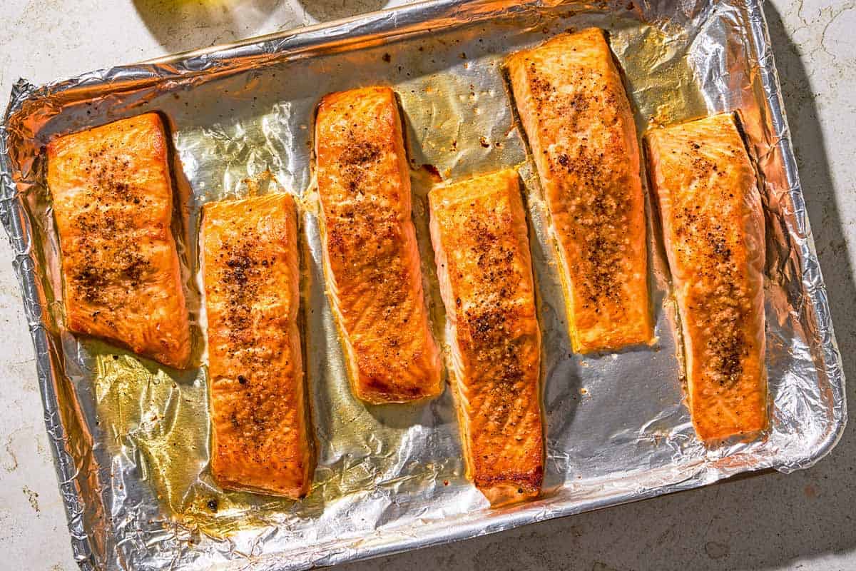 Six baked salmon fillets on a foil lined sheet pan.