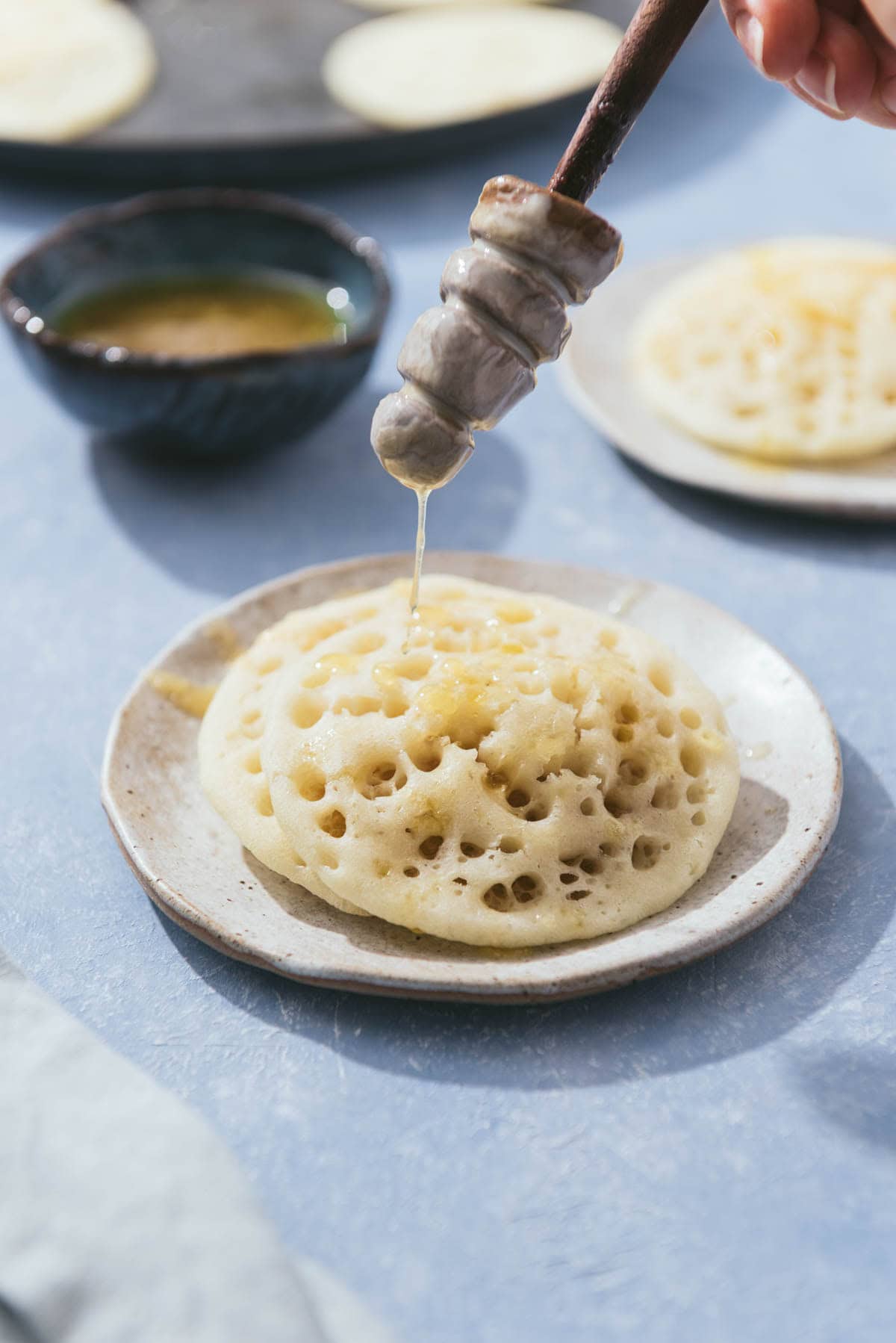 Honey being drizzled on 2 baghrir on a plate.