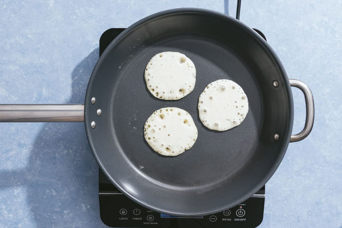 Three baghrir being cooked in a skillet.