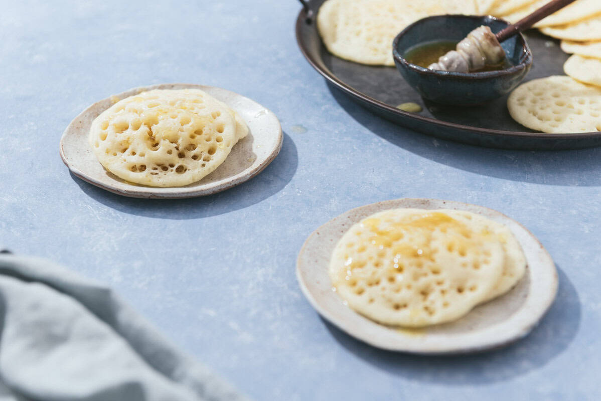 Two plates each with 2 baghrir next to the rest of the baghrir and a bowl of the honey butter mixture on a serving platter.