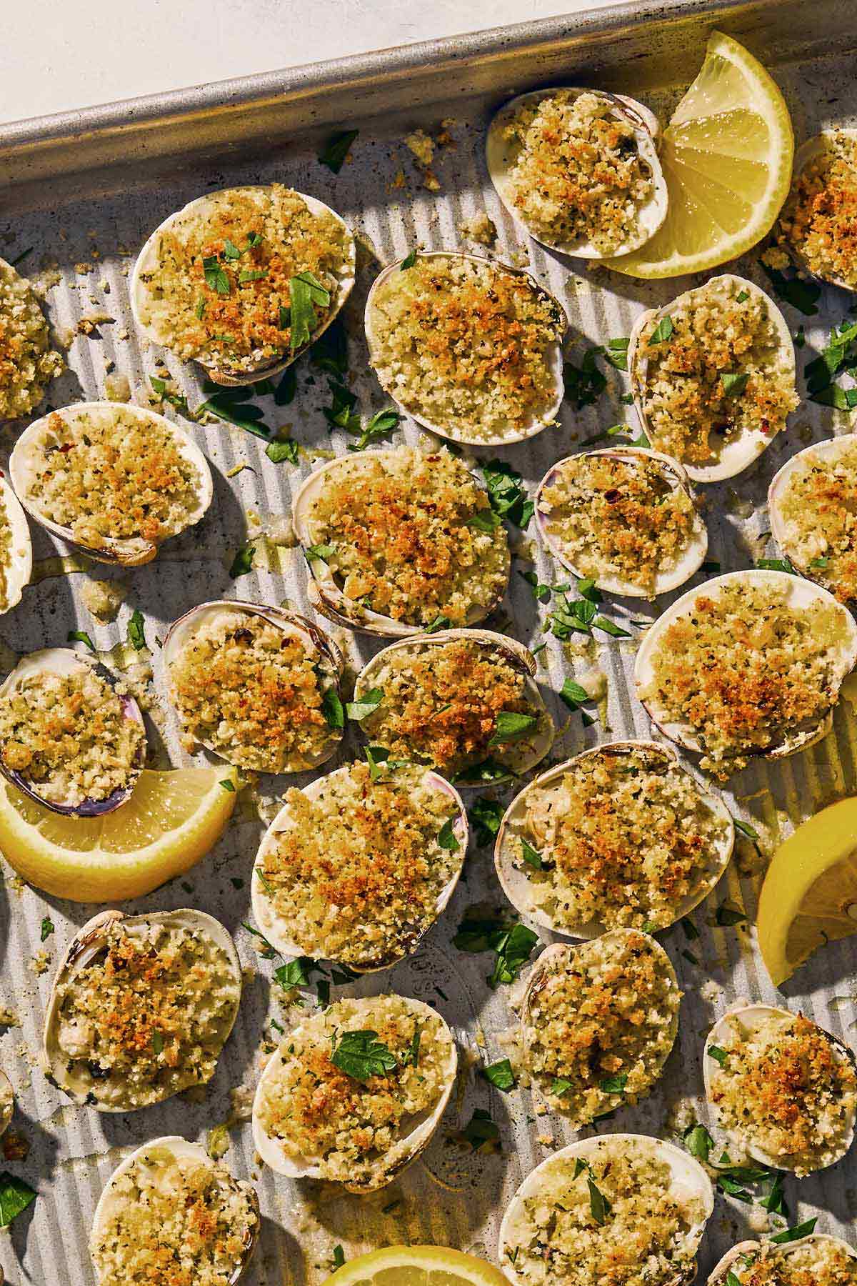 Clams oreganata on a sheet pan with lemon wedges.