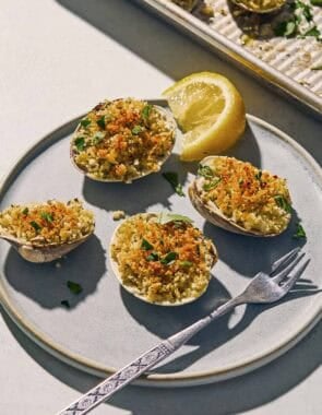 Clams oreganata on a plate with a fork and a lemon wedge.