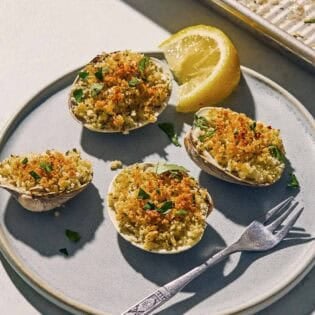 Clams oreganata on a plate with a fork and a lemon wedge.