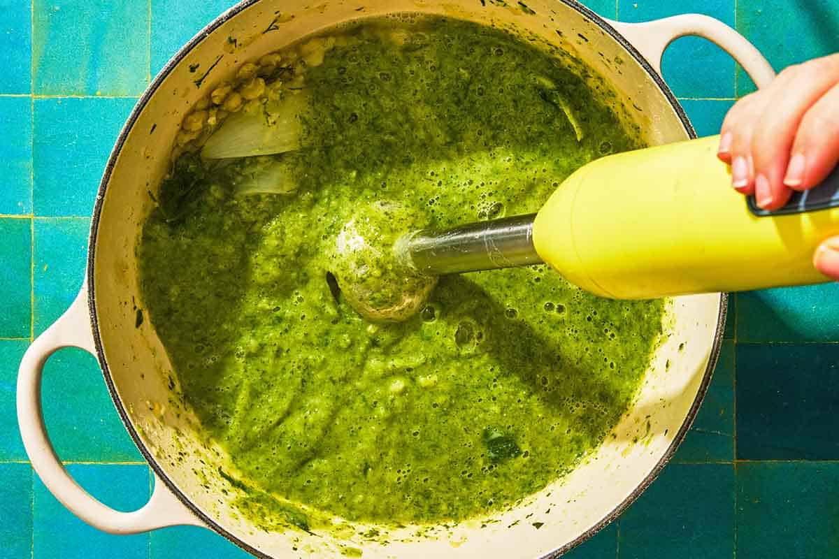 The fava beans, onions, garlic and herbs for the fava bean dip being blended with an immersion blender in a pot.