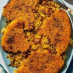 Loobia polo on a platter with a serving spoon. Next to this is a bowl of sliced radishes and a bowl of yogurt.