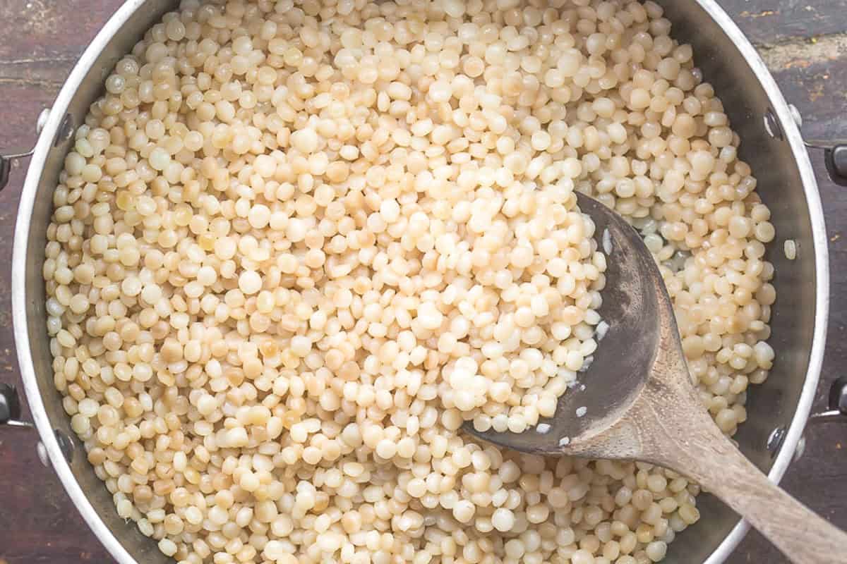 Cooked couscous in a saucepan with a wooden spoon.