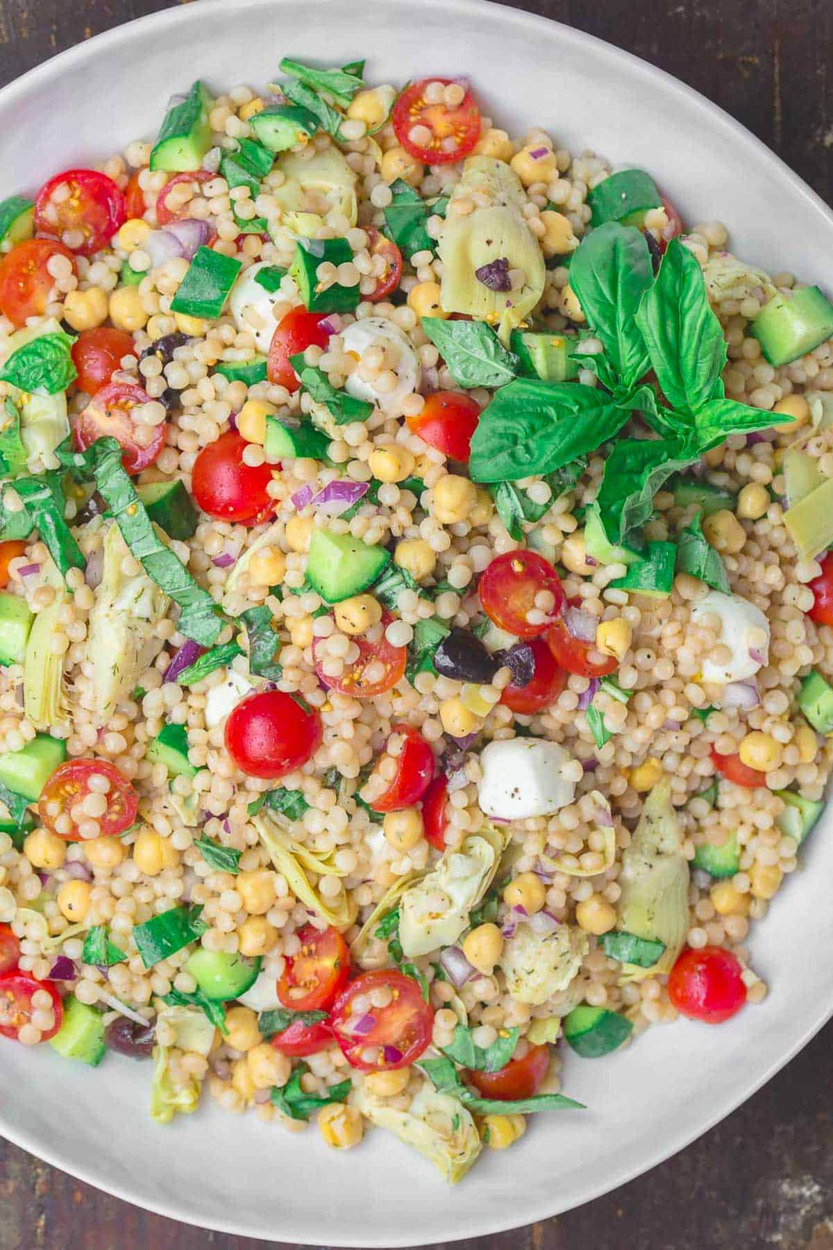 Mediterranean pearl couscous salad with tomatoes, cucumbers, and chickpeas in a white serving bowl.