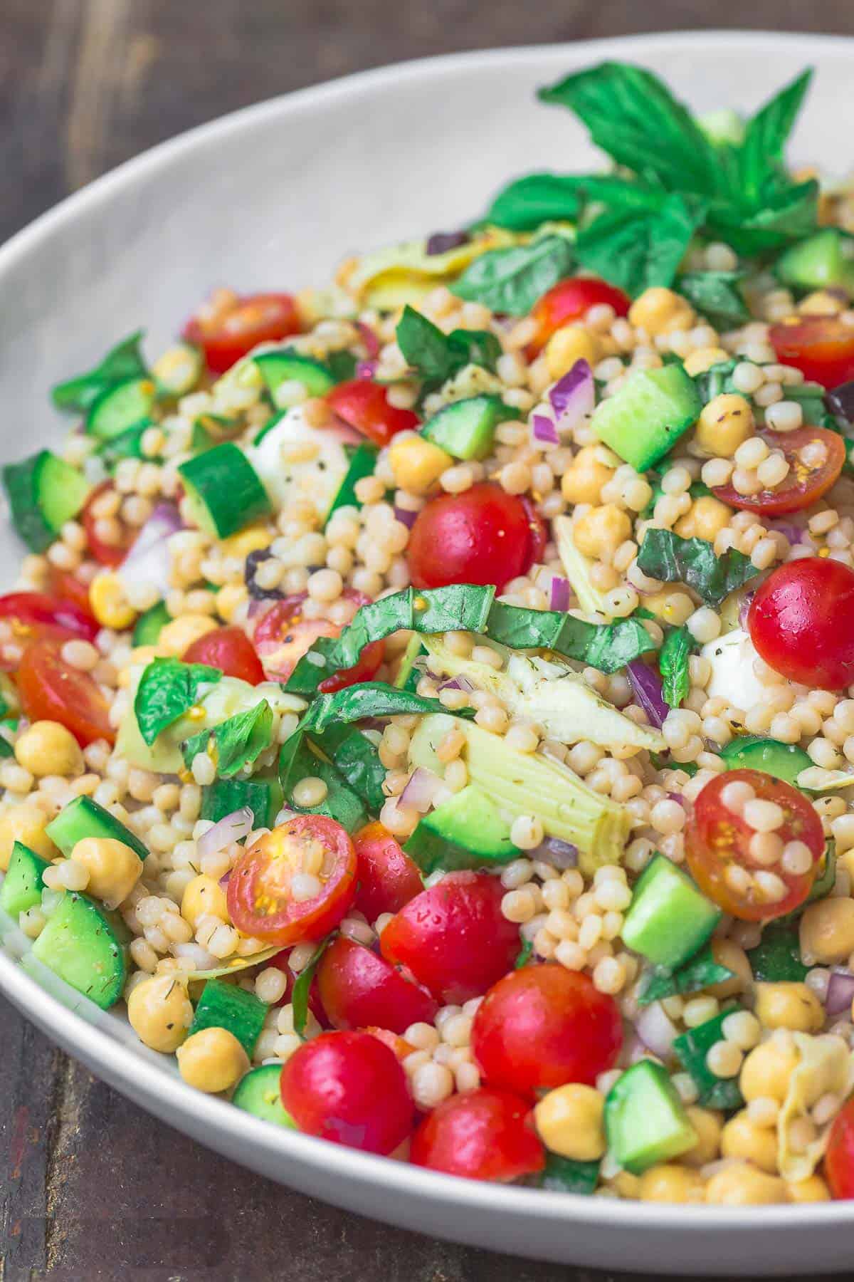 Mediterranean pearl couscous salad with tomatoes, cucumbers, and chickpeas in a white serving bowl.