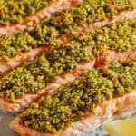 Four pistachio crusted salmon fillets on a platter with lemon wedges.